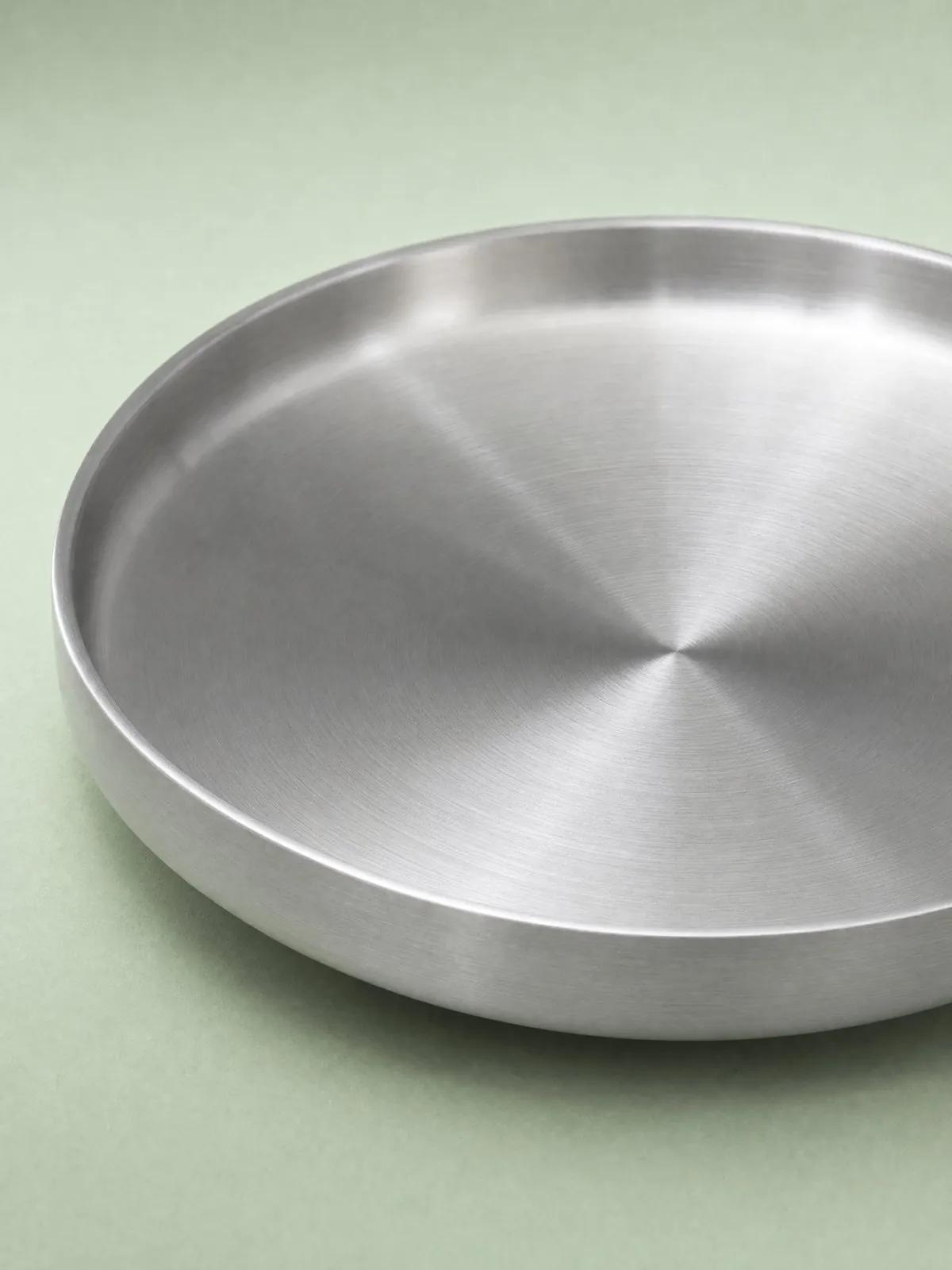 Double-walled brushed stainless steel plate with a high, straight rim on a sage-green background