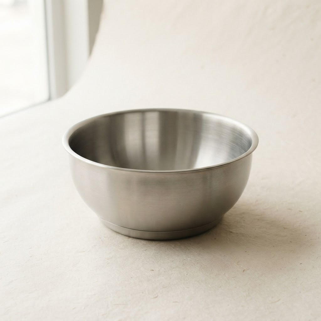 Large deep brushed stainless steel serving bowl on a warm off-white background